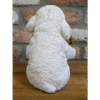 Cute white dog figurine with a basket, sitting on a wooden surface against a brick wall background.