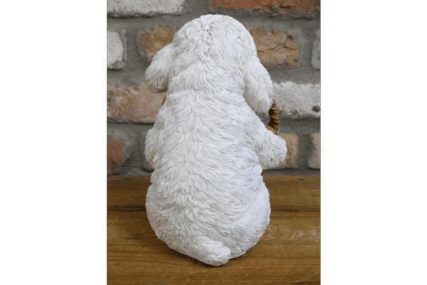 Cute white dog figurine with a basket, sitting on a wooden surface against a brick wall background.