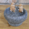 Small dog trough made of textured stone with two small dog figurines inside, placed on a wooden surface.