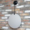 Round hanging mirror with black wall mount on a brick wall, modern home decor.
