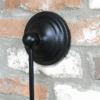 Close-up of a black round hanging mirror with a hook, mounted on a textured brick wall.