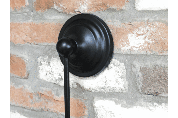Close-up of a black round hanging mirror with a hook, mounted on a textured brick wall.