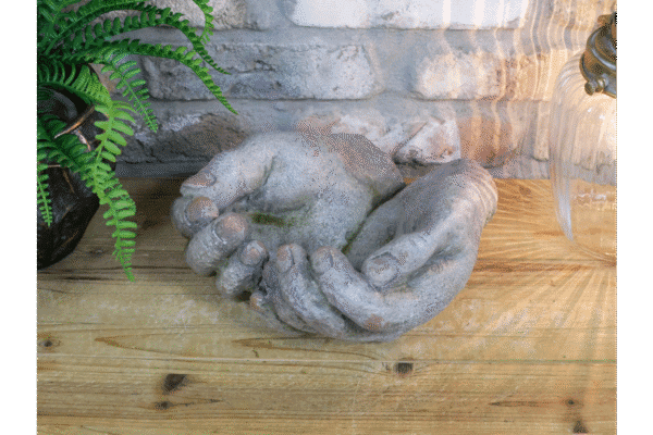 Weathered hands ornament made of stone, placed on a wooden surface with a brick wall background, suitable for home decorating.