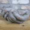 Weathered hands ornament made of textured, aged material, displayed on a wooden surface with a brick wall background.