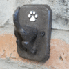 Dog coat hook mounted on a brick wall, featuring a paw print design and a black metal hook for hanging dog accessories.