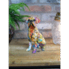 Decorative dog figurine with colourful graffiti-style art sitting on a wooden surface near a green fern and a glass lantern.