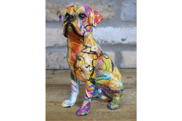 Colourful graffiti-style painted dog sculpture sitting on a wooden surface against a brick wall background.