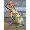 Colourful graffiti-style painted dog sculpture sitting on wooden surface against brick wall background.