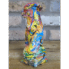 Colourful graffiti-style dog sculpture with vibrant paint splashes and abstract designs, placed on a wooden surface against a brick wall background.