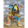 Colourful graffiti-style dog sculpture with vibrant paint splashes and abstract patterns, sitting on a wooden surface against a brick wall background.