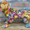 Colourful graffiti-style dog sculpture with vibrant paint splashes on a brick wall background.