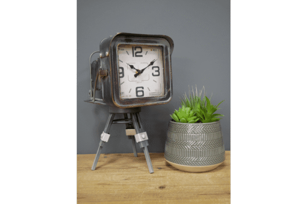 Vintage camera clock with tripod stand next to a potted green succulent plant on a wooden surface.