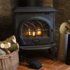 Traditional cast iron wood stove with glowing fire, set in a cozy room with brick flooring and wicker basket of logs.