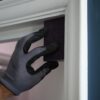 Close-up of a hand wearing a grey glove applying a black sanding sponge to a white door frame for smooth finishing.