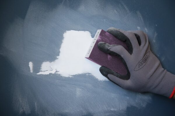 Close-up of a hand wearing a glove using a sanding block on a wall surface for home decorating.