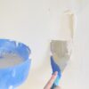 Person applying filler with a putty knife on a wall in a home decorating project.