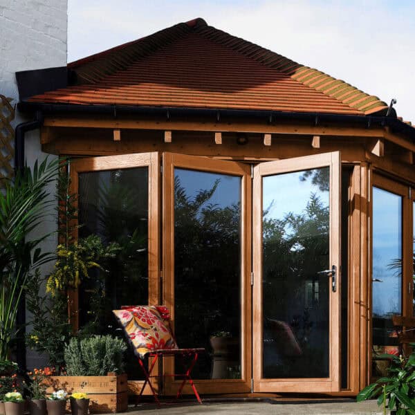 Beautiful wooden conservatory with large glass doors and surrounding lush greenery, ideal for outdoor living and garden enjoyment.
