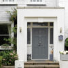 Stylish grey front door with house number 62, flanked by wall-mounted lights and surrounded by lush greenery and flowers.