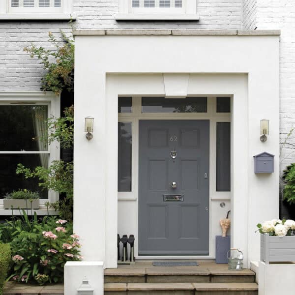 Stylish grey front door with house number 62, flanked by wall-mounted lights and surrounded by lush greenery and flowers.