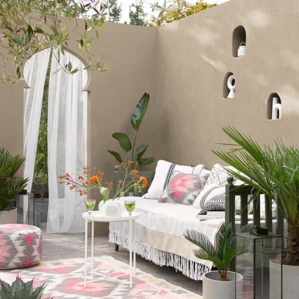 Stylish outdoor patio with beige walls, lush green plants, and comfortable seating for relaxing or entertaining.