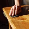 Close-up of a person sanding a wooden surface to prepare for refinishing, highlighting the wood grain and smooth texture.