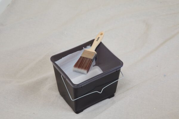Black plastic paint scuttle with reinforced handle and ridged inner base scuttle with brush and paint inside.