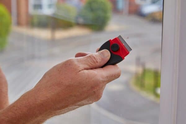 ProDec Razor Edge Window Scraper scraping a glass surface – ergonomic handle and replaceable blade for light paint and residue removal.